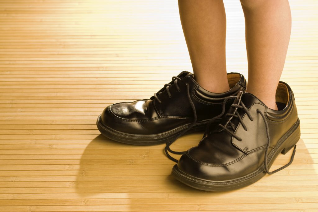 Big shoes to fill, child's feet in large grown-up black shoes, on backlit wood floor, playing dress-up
